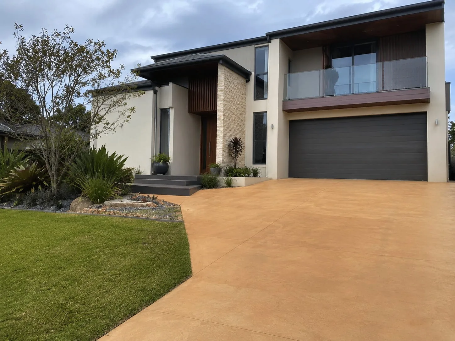 Warm terracotta coloured concrete driveway curving to the garage of a contemporary Newcastle home