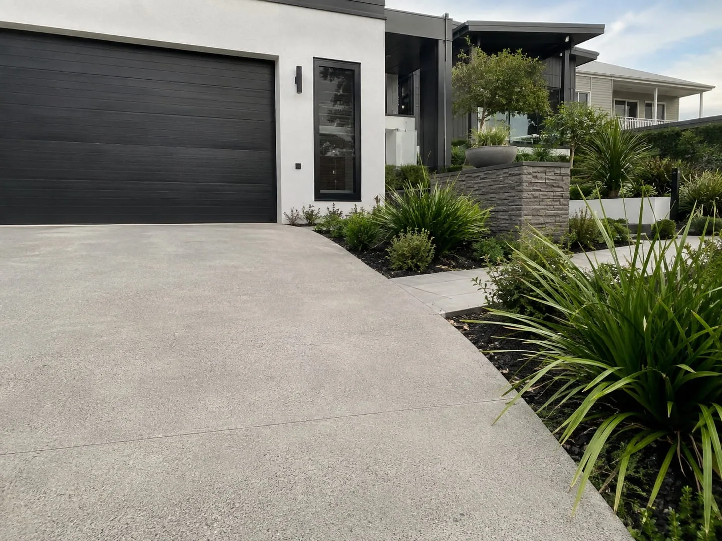 Restored concrete driveway and apron in front of a dark double garage with native grasses alongside